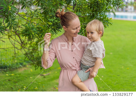 A mother walking with her young son in a sunny park, enjoying quality family time outdoors. Loving connection, parent child bonding, leisure, nature and peaceful everyday moments concept 133829177