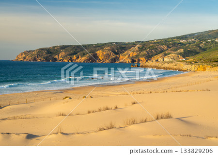 Guincho Beach, Sand Dunes, Green Hills and Cliffs in Evening. Atlantic Ocean, Portugal Guincho Beach, Sand Dunes, Green Hills and Cliffs in Evening. Atlantic Ocean, Portugal 133829206