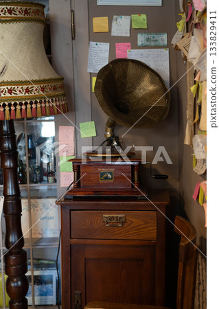 In a cozy corner, an elegant vintage gramophone rests atop a wooden cabinet. Colorful notes decorate the wall, hinting at cherished memories. 133829411
