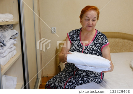 Woman folding laundry mature old woman with red hair Female dry cleaning worker folding clean laundry and preparing for delivery. Woman folding laundry mature old woman with red hair Female dry cleaning worker folding clean laundry and preparing for delivery. 133829468