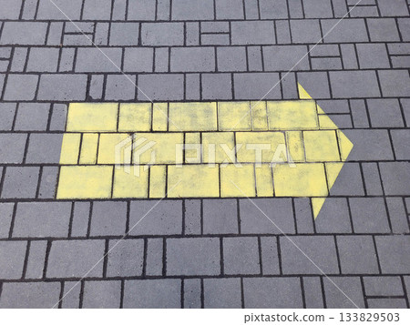 A yellow arrow sign is painted on the gray tile sidewalk A yellow arrow sign is painted on the gray tile sidewalk 133829503