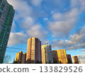 On a sunny day, modern buildings with many windows and balconies stand against a blue sky with clouds. 133829526