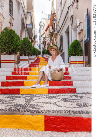 Young woman in a white dress sitting on the colourful Spanish Steps in the Arrabal old town district of Calpe, Spain Young woman in a white dress sitting on the colourful Spanish Steps in the Arrabal old town district of Calpe, Spain 133829779