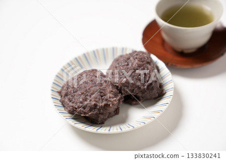 白盤子裡放著兩個飯糰和一杯茶。 133830241