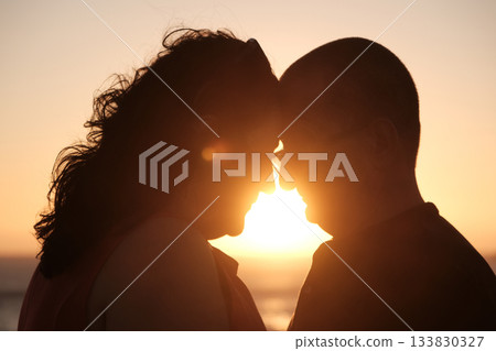 Mature couple touching foreheads in a tender moment at sunset with warm golden light creating a romantic silhouette. Mature couple touching foreheads in a tender moment at sunset with warm golden light creating a romantic silhouette. 133830327