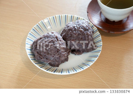 白盤子裡放著兩個飯糰和一杯茶。 133830874