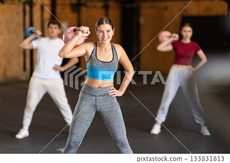 Girl in gym does exercises with kettlebell, lifts and lowers heavy kettlebell with one hand Girl in gym does exercises with kettlebell, lifts and lowers heavy kettlebell with one hand 133831813