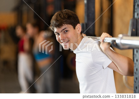 Slender guy trains muscles of arms and back using barbell and differentiated weighting in gym Slender guy trains muscles of arms and back using barbell and differentiated weighting in gym 133831818