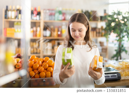 Teen girl hold packages bottles and choose consider juice in store Teen girl hold packages bottles and choose consider juice in store 133831851