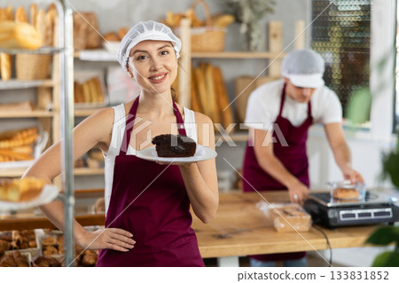 Young saleswoman holding piece of pastry in paper plate Young saleswoman holding piece of pastry in paper plate 133831852