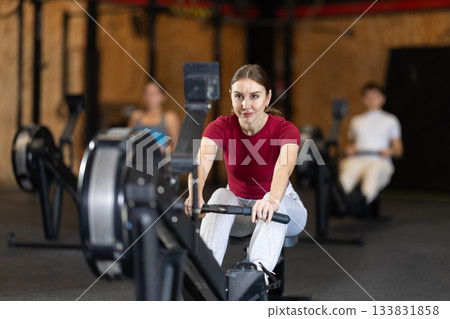 Focused girl works out with rowing machine during class at fitness club 133831858