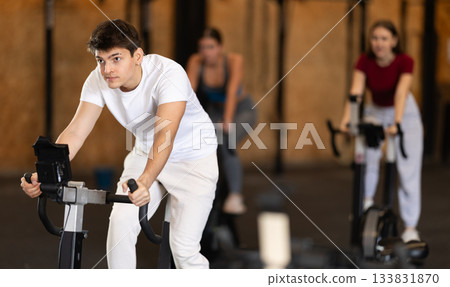 Focused guy works out with exercise bicycle during class at fitness club Focused guy works out with exercise bicycle during class at fitness club 133831870