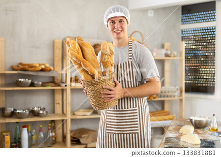 In working room of bakery, there is man with baguettes in wicker basket in hands In working room of bakery, there is man with baguettes in wicker basket in hands 133831881