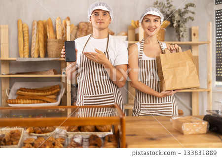 Salesman displays phone app standing next to saleswoman with paper bag 133831889