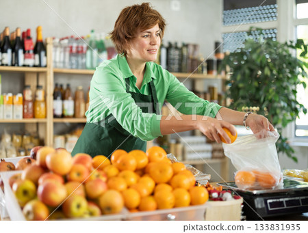 Adult woman seller weighs tangerines in grocery store Adult woman seller weighs tangerines in grocery store 133831935