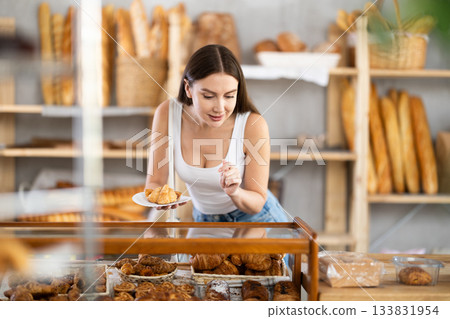 Satisfied female customer selects fresh croissants at display window of bakery 133831954