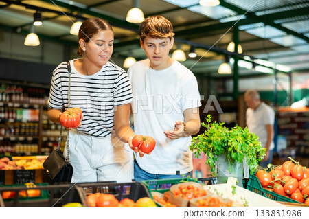 Cheerful young couple choosing ripe red tomatoes in store 133831986