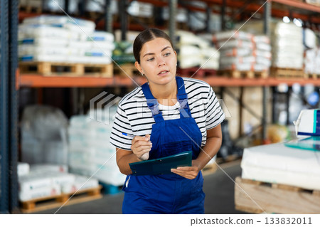 In warehouse of store, girl checks quantity of goods and receipt documents for products In warehouse of store, girl checks quantity of goods and receipt documents for products 133832011