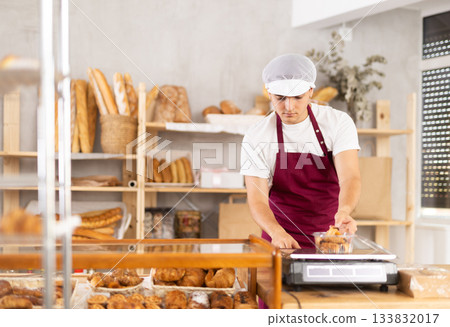 Young baker weighs fresh croissants on a scale and places them in plastic container Young baker weighs fresh croissants on a scale and places them in plastic container 133832017