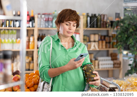 Woman customer holds jar of canned cucumber in hand, scans QR code on product label 133832095