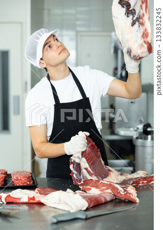 Positive young salesman demonstrating piece of meat in butcher shop Positive young salesman demonstrating piece of meat in butcher shop 133832245