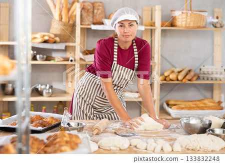 Adult female baker kneading dough on table 133832248