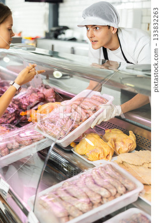 Positive young salesman demonstrating container with sausages in butcher shop Positive young salesman demonstrating container with sausages in butcher shop 133832263