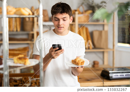 Interested guy using smartphone to analyze pastry in bakery 133832267