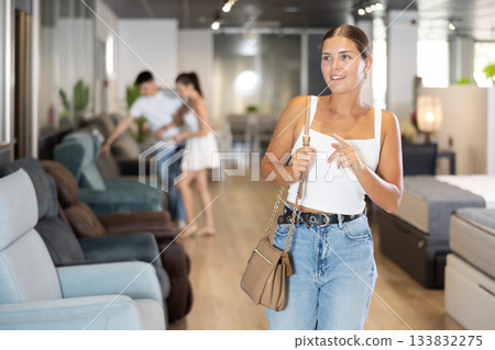 Girl buyer noticed desired product in furniture store and smiles joyfully at upcoming purchase 133832275