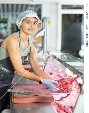 Positive young saleswoman demonstrating piece of meat in butcher shop Positive young saleswoman demonstrating piece of meat in butcher shop 133832279