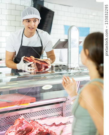 Young male seller offers girl to buy fresh beef entrecote boneless meat 133832295
