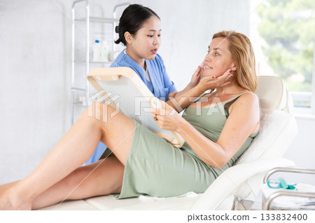 Professional cosmetologist talking about anti-aging skincare to patient Professional cosmetologist talking about anti-aging skincare to patient 133832400