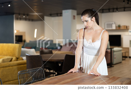 Woman choosing dining table in furniture store, looking at various samples on display with interest Woman choosing dining table in furniture store, looking at various samples on display with interest 133832408