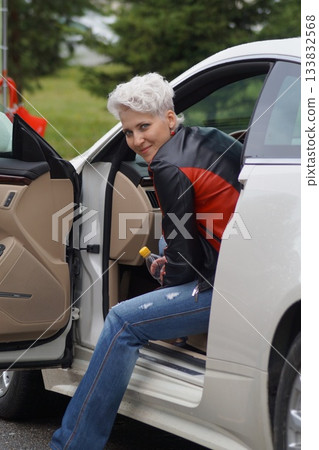 One girl, a blonde, is sitting in an expensive car and looking into the distance. It's autumn and raining outside. 133832568