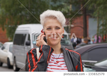 A blonde girl with model-like looks is walking down the street and talking on the phone. She is smiling and happy A blonde girl with model-like looks is walking down the street and talking on the phone. She is smiling and happy 133832570