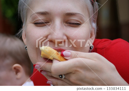 One blonde girl bites and eats pizza, she closed her eyes with pleasure and smiles. 133834111
