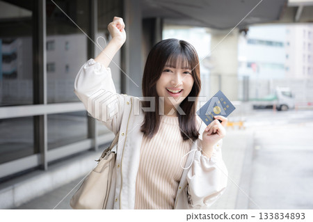 一位微笑的女士在機場和車站拿著護照。讓我們一起出國旅行吧！她看向鏡頭。 133834893