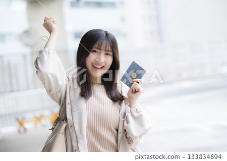 一位微笑的女士在機場和車站拿著護照。讓我們一起出國旅行吧！她看向鏡頭。 133834894