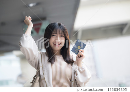 一位微笑的女士在機場和車站拿著護照。讓我們一起出國旅行吧！她看向鏡頭。 133834895