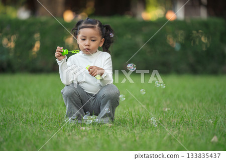 happy toddler girl blowing soap bubbles in park happy toddler girl blowing soap bubbles in park 133835437