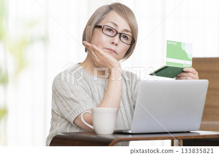 A senior woman staring at her bankbook and computer in the living room A senior woman staring at her bankbook and computer in the living room 133835821