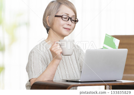 A senior woman staring at her bankbook and computer in the living room A senior woman staring at her bankbook and computer in the living room 133835829