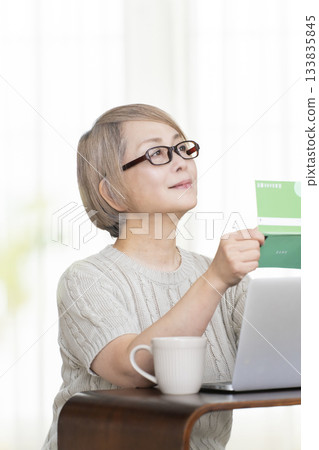 一位老婦人在客廳裡盯著她的存摺和電腦。 133835845