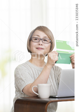 一位老婦人在客廳裡盯著她的存摺和電腦。 133835846