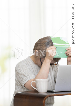 一位老婦人在客廳裡盯著她的存摺和電腦。 133835847