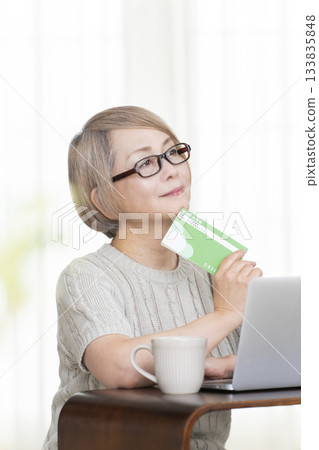 一位老婦人在客廳裡盯著她的存摺和電腦。 133835848