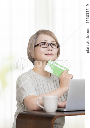 一位老婦人在客廳裡盯著她的存摺和電腦。 133835849