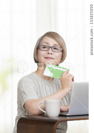 一位老婦人在客廳裡盯著她的存摺和電腦。 133835850