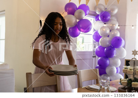 African American child in pink dress arranging plates on table under balloon arch in dining room African American child in pink dress arranging plates on table under balloon arch in dining room 133836164
