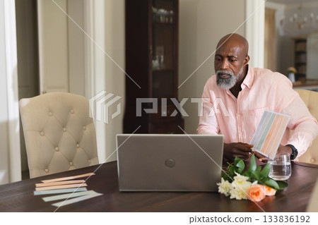 Senior African American man reviewing color swatches at table with laptop and flowers, copy space 133836192